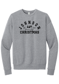Personalized Family Christmas crewneck sweatshirt in Athletic Heather, featuring an arched family name over pine trees with EST. year and family Christmas lettering