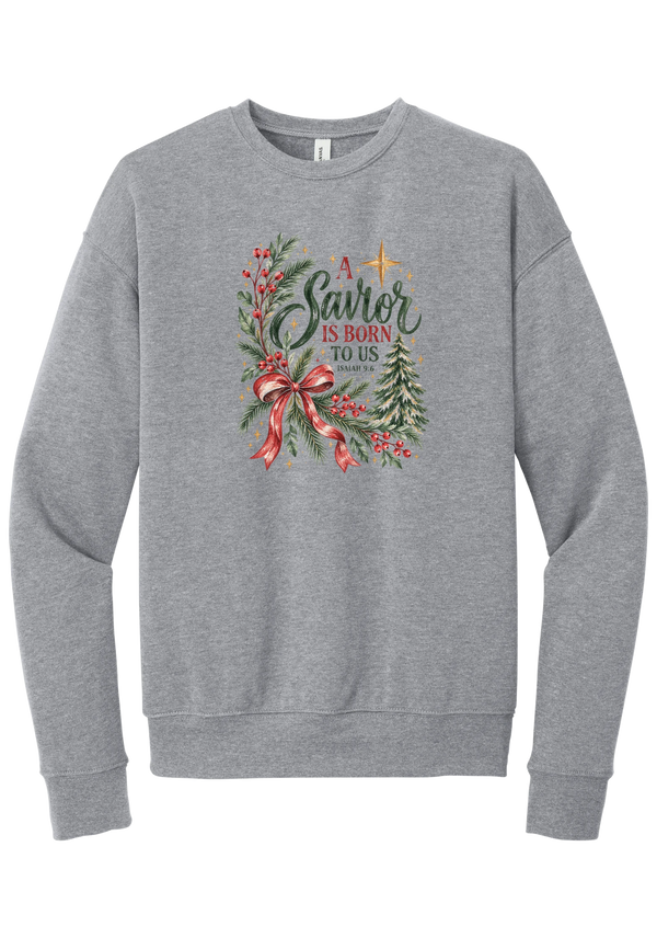 A Savior Is Born To Us crewneck sweatshirt in Athletic Heather, featuring watercolor evergreen and holly with a red ribbon bow, the words A Savior is born to us, and Isaiah 9:6