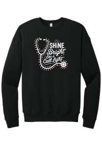 Shine Bright Like a Call Light crewneck sweatshirt in Black, featuring a white stethoscope wrapped in multicolor Christmas lights with Shine Bright Like a Call Light lettering and sparkles