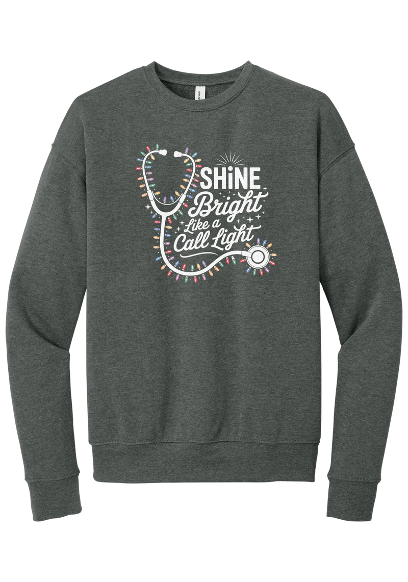 Shine Bright Like a Call Light crewneck sweatshirt in Deep Heather, featuring a white stethoscope wrapped in multicolor Christmas lights with Shine Bright Like a Call Light lettering and sparkles