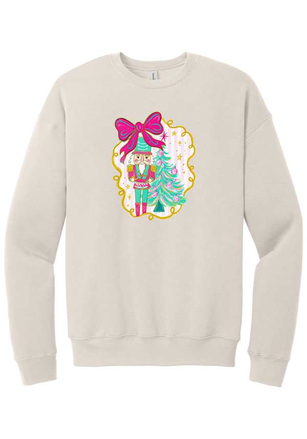 Nutcracker Bow crewneck sweatshirt in Heather Dust, featuring a teal and pink nutcracker beside a tinsel tree under a big hot pink bow