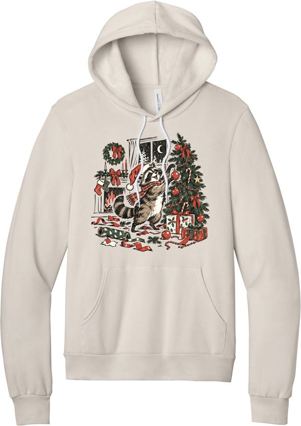 Raccoon Christmas hoodie in Heather Dust, featuring a vintage-style raccoon in a Santa hat and plaid scarf decorating a Christmas tree by the fireplace with ribbon and gifts scattered around