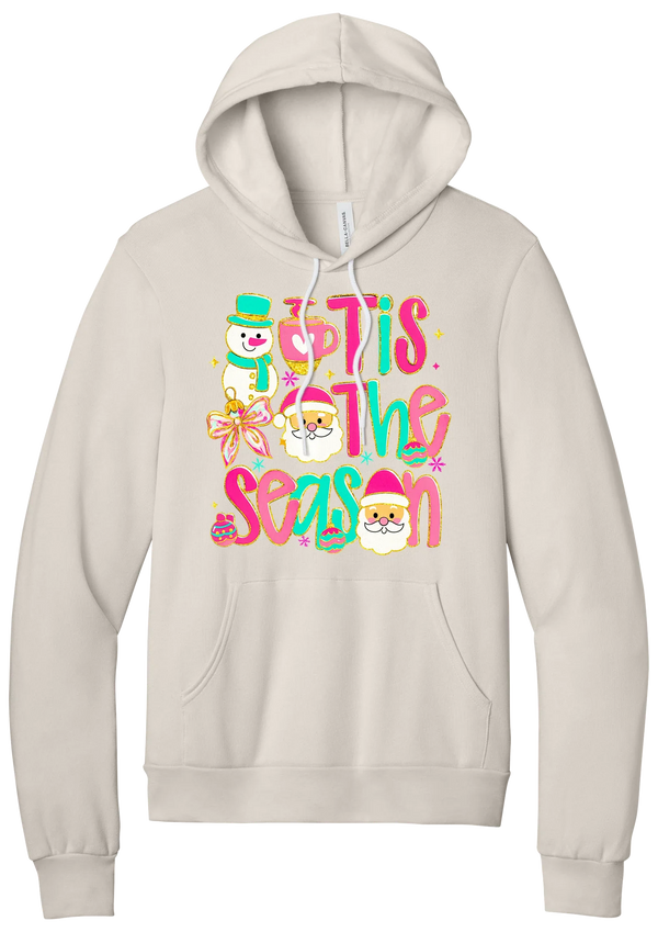 Tis the Season Snowman hoodie in Heather Dust, featuring pink and teal TIS THE SEASON letters with a snowman, a cocoa mug, and Santas