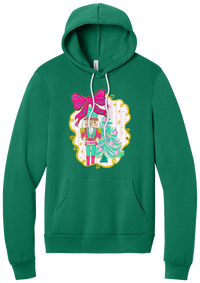 Nutcracker Bow hoodie in Kelly Green, featuring a teal and pink nutcracker beside a tinsel tree under a big hot pink bow
