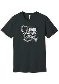 Shine Bright Like a Call Light tee in Dark Grey, featuring a white stethoscope wrapped in multicolor Christmas lights with bold Shine Bright Like a Call Light lettering