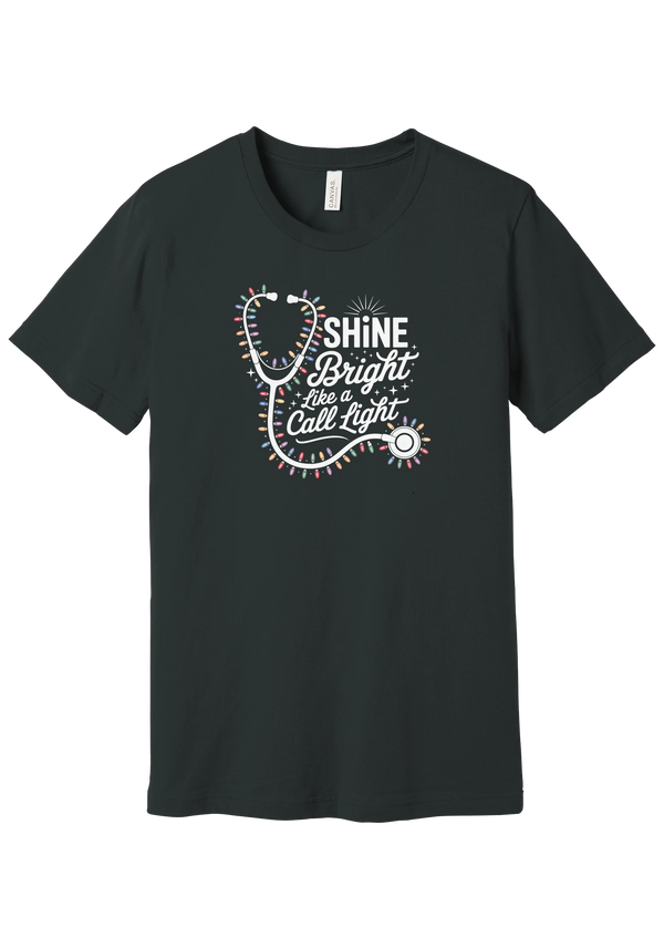 Shine Bright Like a Call Light tee in Dark Grey, featuring a white stethoscope wrapped in multicolor Christmas lights with bold Shine Bright Like a Call Light lettering