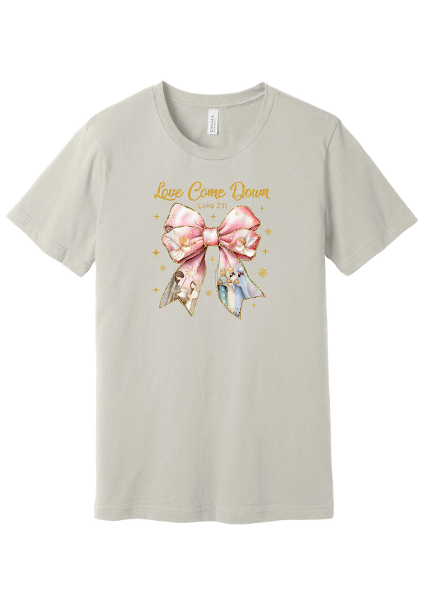 Love Came Down Nativity Bow tee in Dust, featuring a blush satin bow with painted nativity scenes under gold Love Came Down script and Luke 2:11