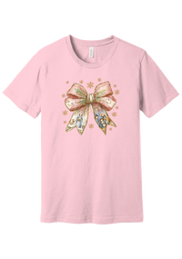 Nativity Bow tee in Pink, featuring a blush satin bow with painted nativity scenes in its ribbons and gold snowflakes