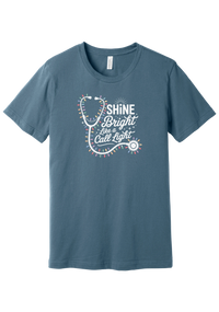 Shine Bright Like a Call Light tee in Steel Blue, featuring a white stethoscope wrapped in multicolor Christmas lights with bold Shine Bright Like a Call Light lettering
