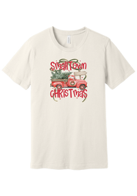 Personalized Small Town Christmas tee in Vintage White, featuring Santa in a vintage red pickup hauling a Christmas tree past a road sign personalized with your town