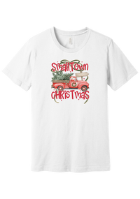 Personalized Small Town Christmas tee in White, featuring Santa in a vintage red pickup hauling a Christmas tree past a road sign personalized with your town